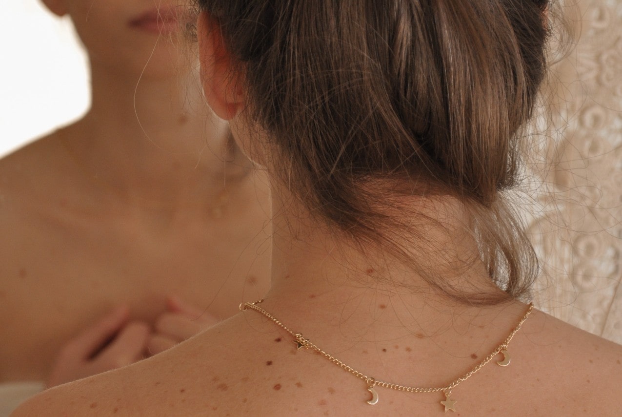 posterior view of a woman wearing a gold chain necklace with moon and star motifs