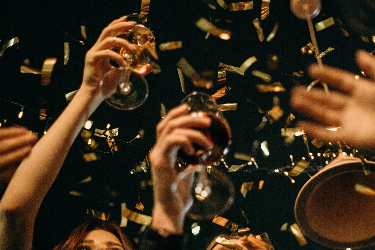 a group raises their wine glasses at night as gold confetti falls from above.