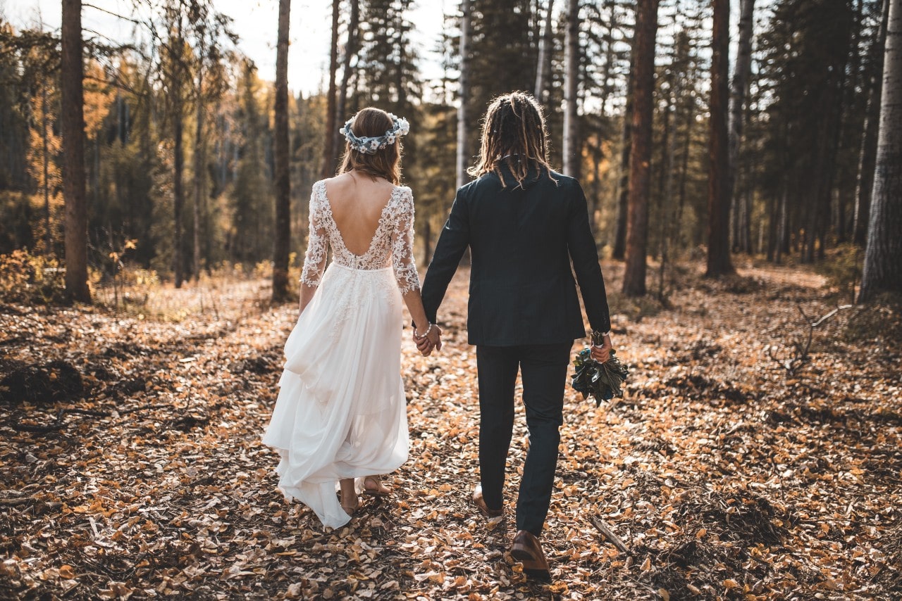 A couple holding hands while walking through a fall forest.