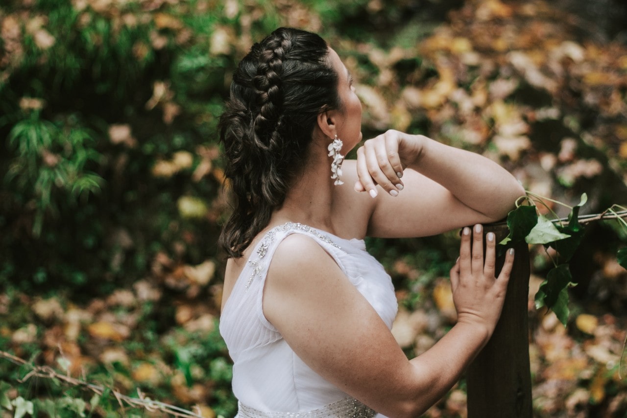 A bride leans against a fence post and looks into the fall landscape.