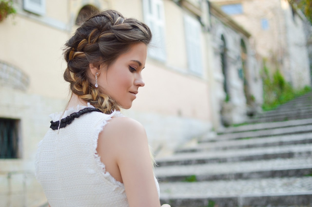 a woman wearing a white tank looks over her shoulder wearing diamond drop earrings.